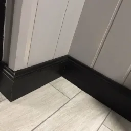 Fragment wykończonego wnętrza: szare panele ścienne z czarnymi listwami przypodłogowymi i jasnymi płytkami podłogowymi imitującymi drewno.