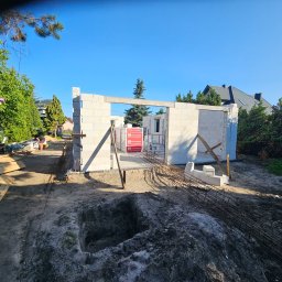 PRODOM MARCIN KOŁAT - Budowa domu: ściany z betonu komórkowego wzniesione, widoczne zbrojenia i palety z bloczkami Termobet. W tle zieleń i błękitne niebo.