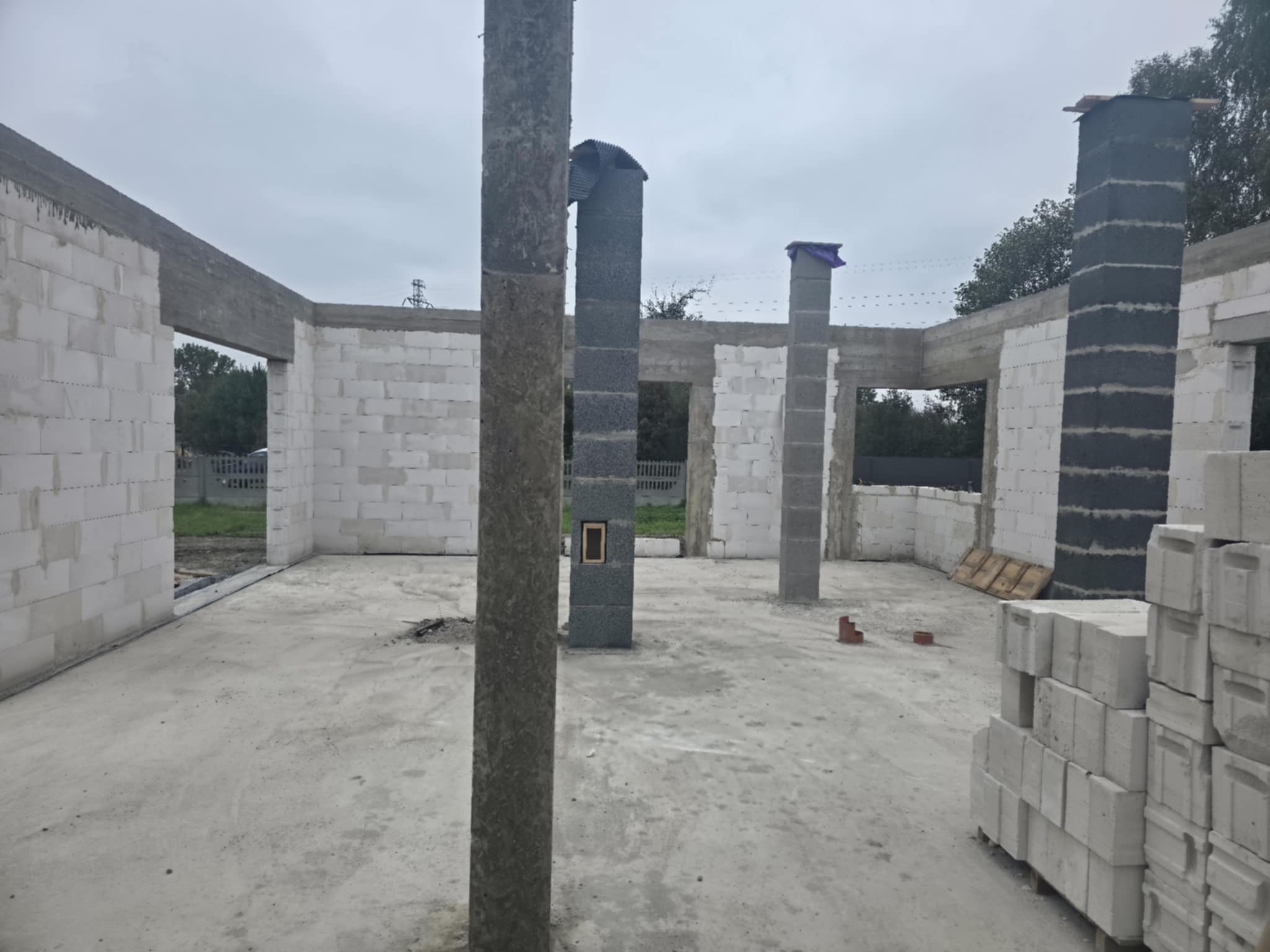 Surowy stan domu z białych bloczków: widoczne filary, ściany w trakcie budowy, surowy beton na podłodze. Etap wznoszenia konstrukcji budynku.