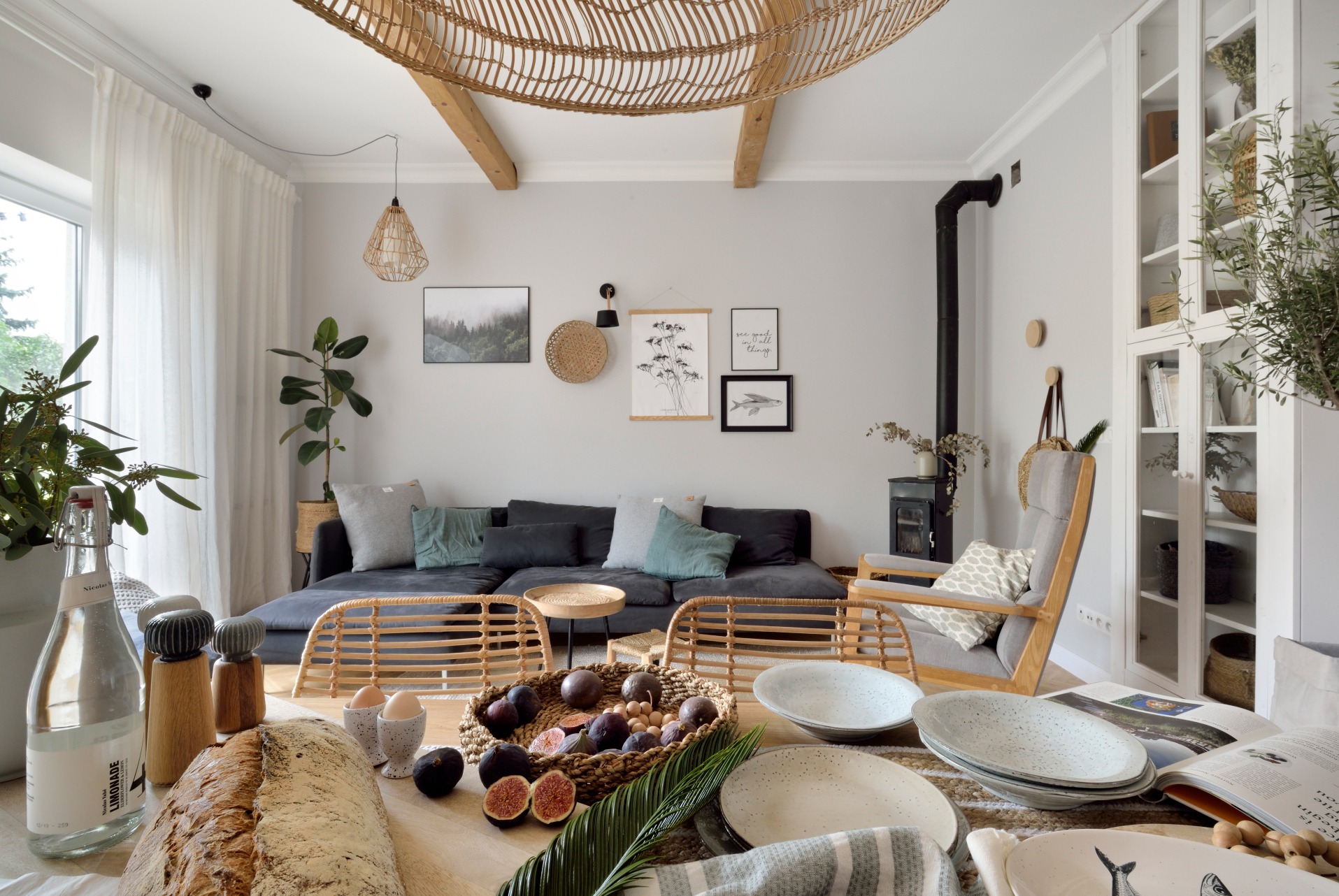 Jasne wnętrze: stół z owocami i naczyniami na pierwszym planie, w tle sofa, kominek i dekoracje w stylu skandynawskim. Wnętrze doświetlone naturalnym światłem.