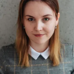 Portret kobiety w koszuli w kratę z białym kołnierzykiem, na tle szarej ściany.