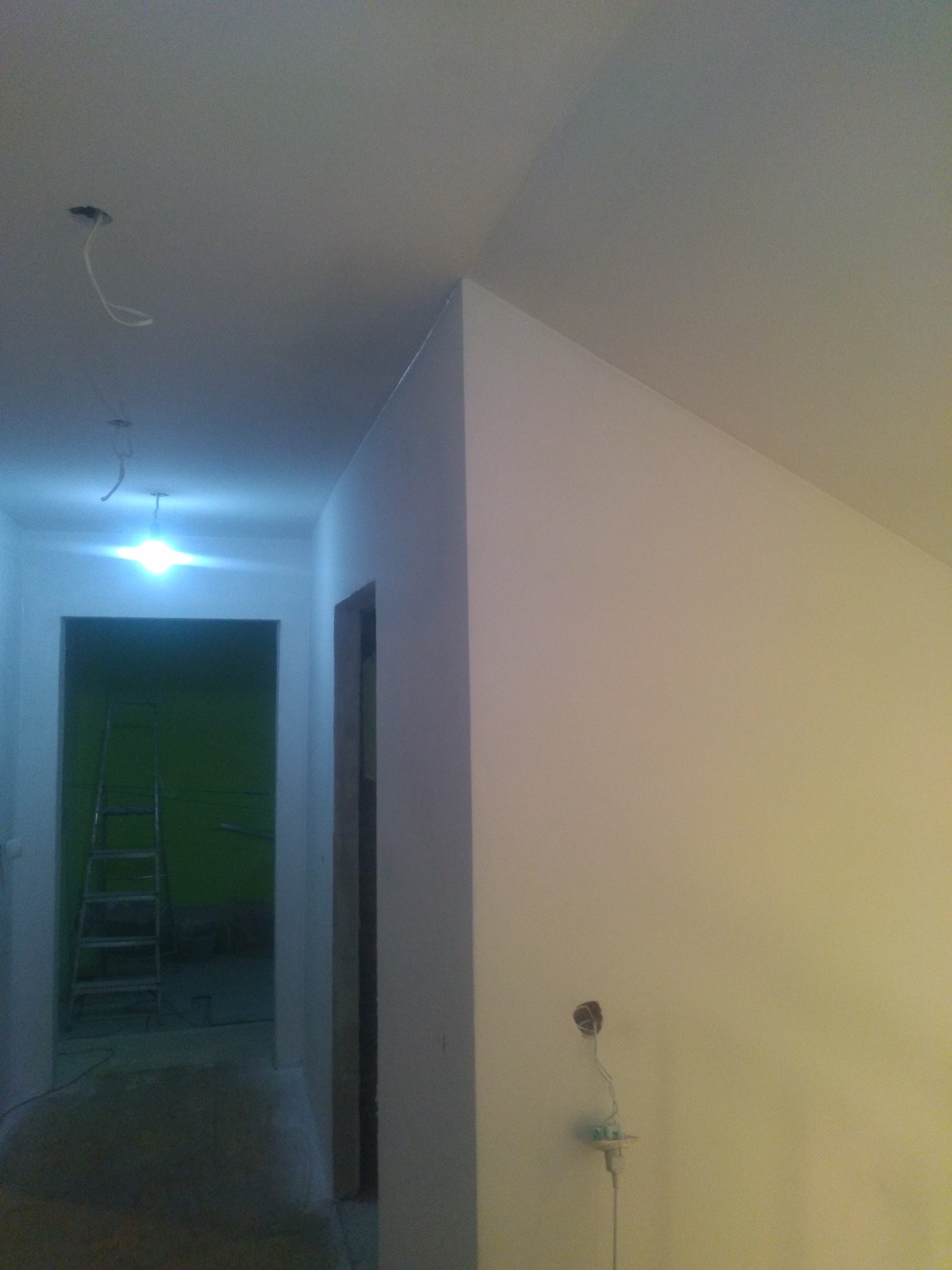 Wnętrze w trakcie prac wykończeniowych: białe ściany, widoczne kable elektryczne, drabina w tle, surowe otwory drzwiowe.