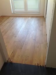 Fragment pokoju z nowo ułożoną, jasną, drewnianą podłogą parkietową w trakcie montażu, widoczne niedocięte elementy i czarna folia podkładowa przy progu.