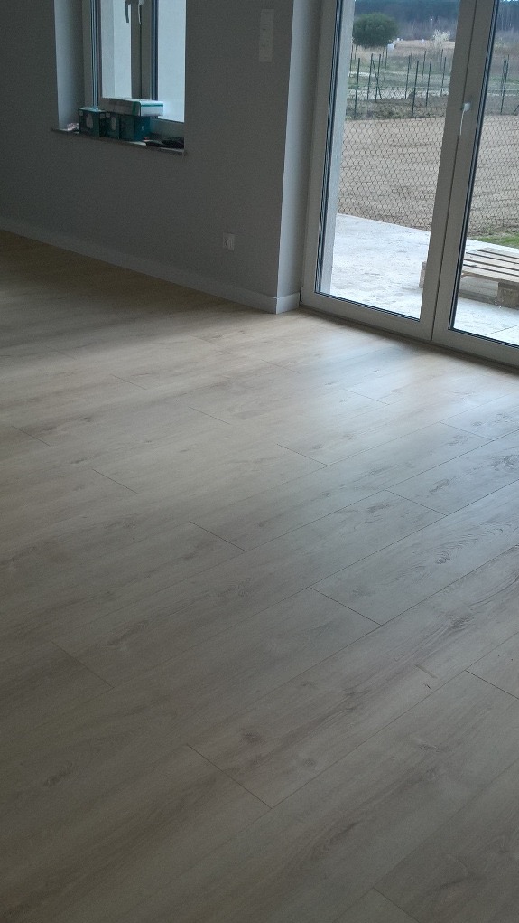 Jasna podłoga z paneli ułożona w nowym domu, widok na okno balkonowe i parapet z pudełkami.