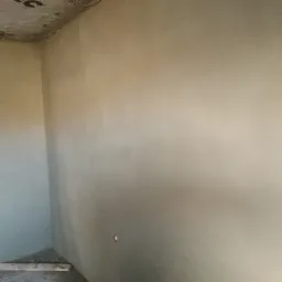 Wnętrze pokoju po nałożeniu świeżej warstwy jasnego tynku na ściany, widoczny fragment sufitu z izolacją i wystający kabel elektryczny.
