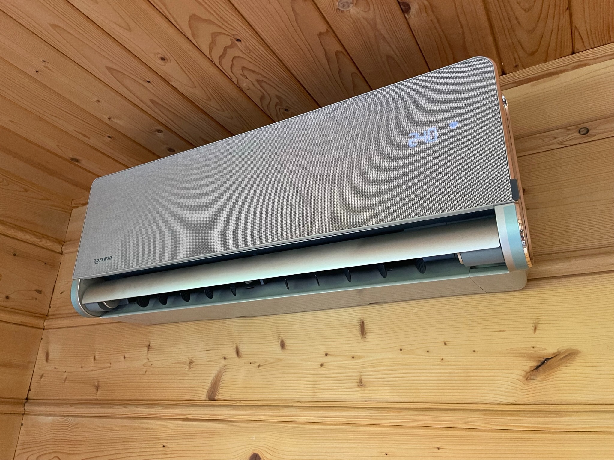 Szary klimatyzator Rotenso zamontowany na drewnianej ścianie z boazerii, wyświetlający godzinę 2:40.