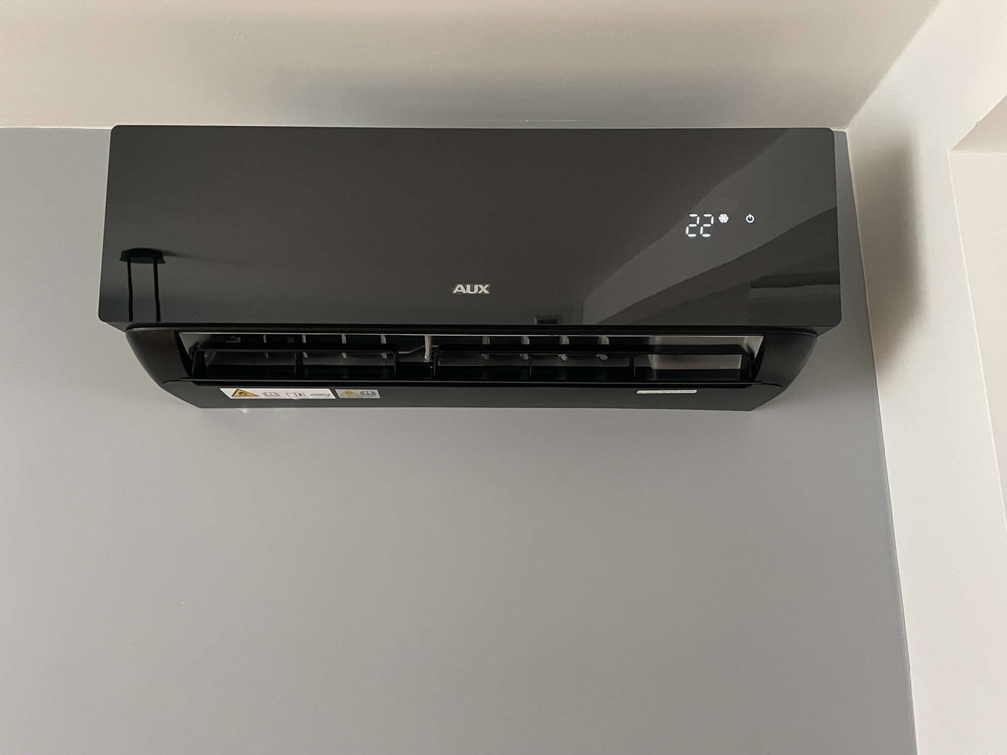 Czarny klimatyzator AUX z wyświetlaczem temperatury (22 stopnie Celsjusza) zamontowany na szarej ścianie w Kluczach.