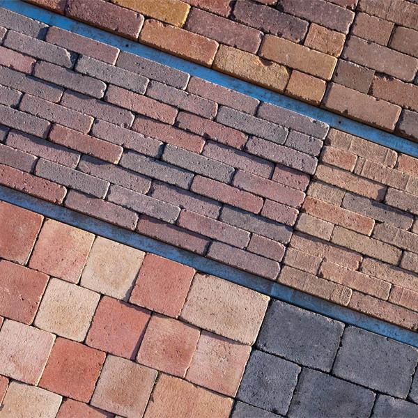 Ekspozycja różnokolorowych kostek brukowych w Górze, prezentująca różne wzory ułożenia i faktury.