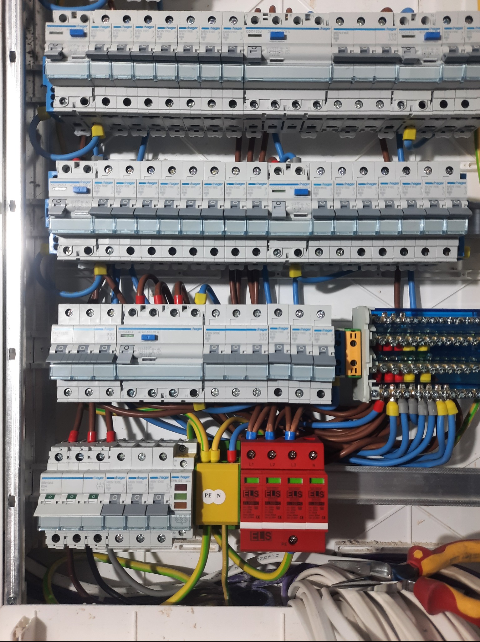 Rozdzielnia elektryczna Hager z zabezpieczeniami przepięciowymi ELS, widoczne bezpieczniki, przewody w kolorach niebieskim, brązowym, żółto-zielonym.