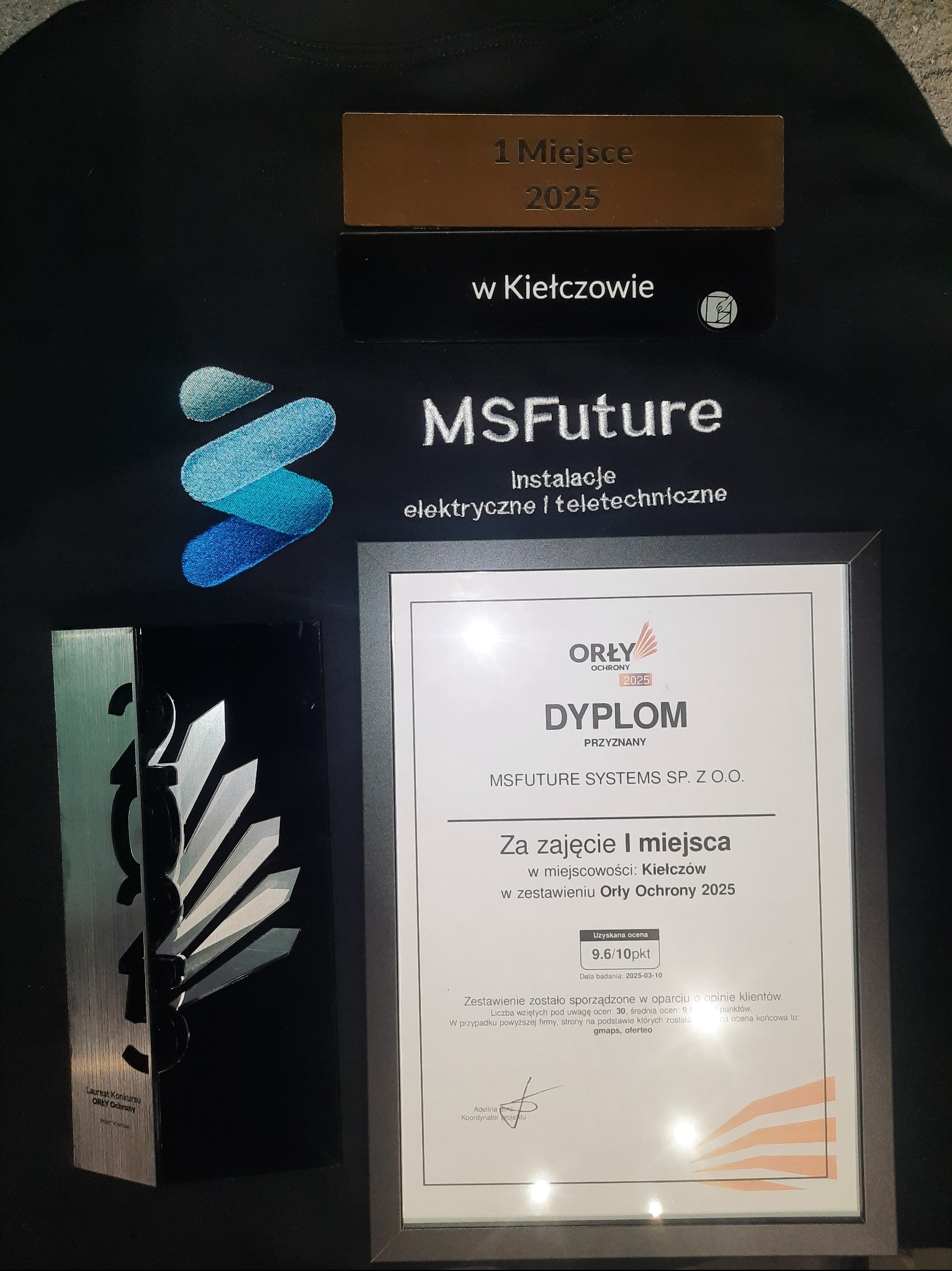 Dyplom 'Orły Ochrony 2025' za I miejsce dla MSFuture Systems, obok statuetka i tabliczka z napisem '1 Miejsce 2025', logo firmy na czarnej koszulce.