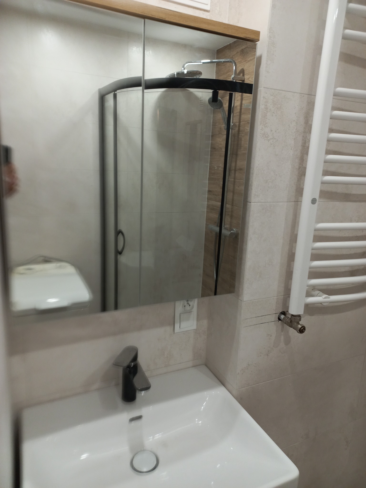 Łazienka z umywalką z czarną baterią, grzejnikiem drabinkowym i kabiną prysznicową widoczną w lustrze.