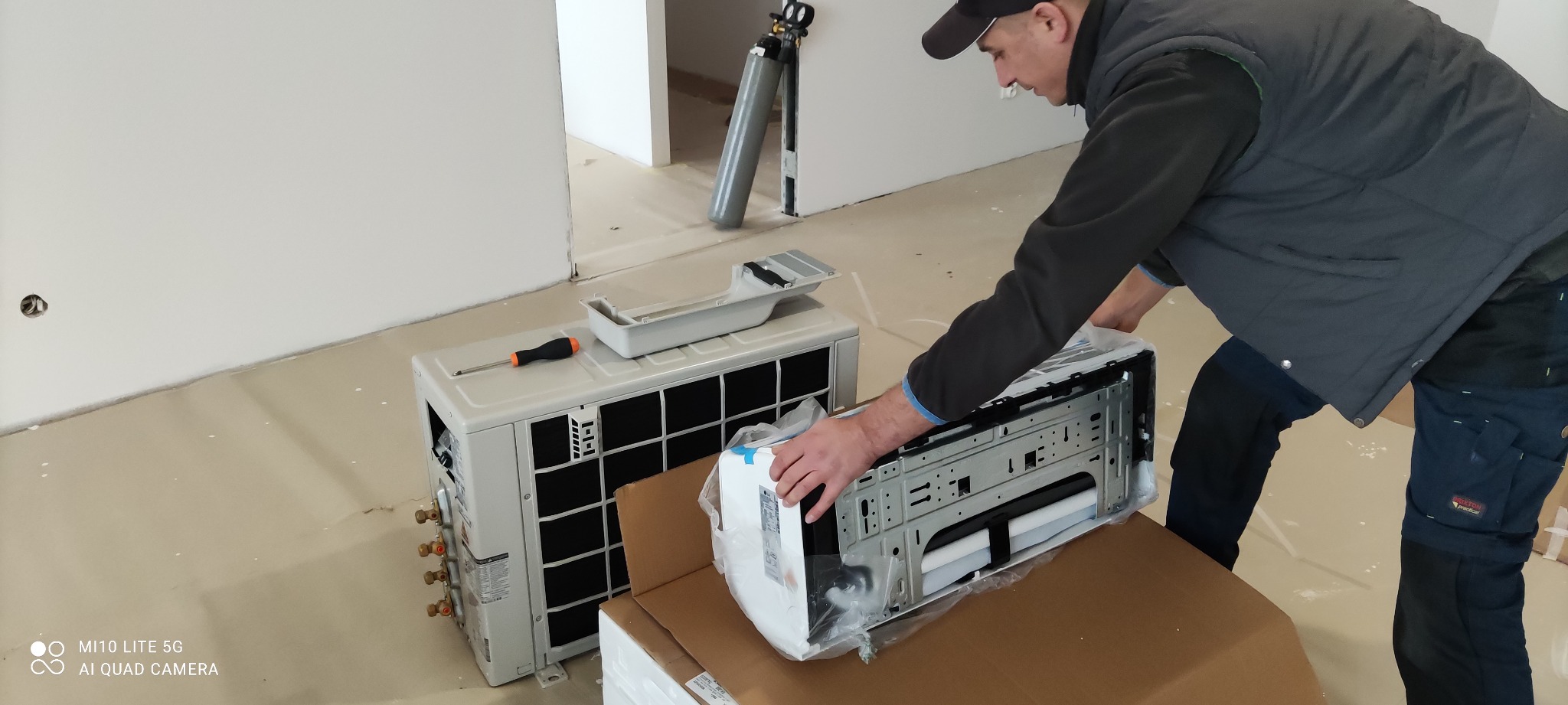 Instalator w kamizelce przygotowuje do montażu jednostkę wewnętrzną klimatyzatora LG, obok jednostka zewnętrzna i butla z gazem chłodniczym.