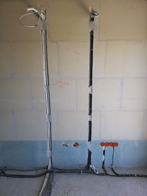 Instalacja elektryczna w trakcie montażu w surowym wnętrzu, widoczne przewody w pionowych bruzdach w ścianie z płyt gipsowo-kartonowych, zabezpieczone taśmą, puszki elektryczne w ścianie, kable...