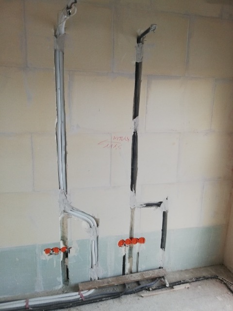 Wewnętrzne instalacje hydrauliczne i elektryczne w ścianie w trakcie montażu, widoczne rury i kable, ściana częściowo wykończona, przygotowane otwory pod osprzęt.