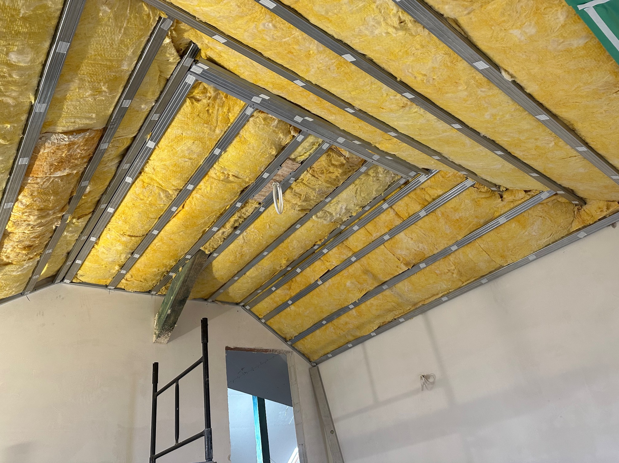 Poddasze w trakcie ocieplania wełną mineralną, widoczne metalowe profile konstrukcyjne, fragment ściany i rusztowania