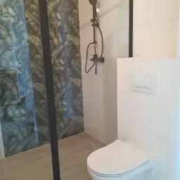 Nowoczesna łazienka z kabiną prysznicową z motywem liści, czarną armaturą i podwieszaną toaletą.