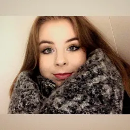 Portret młodej kobiety z długimi, brązowymi włosami i zielonymi oczami, otulonej szarym, wzorzystym szalem.