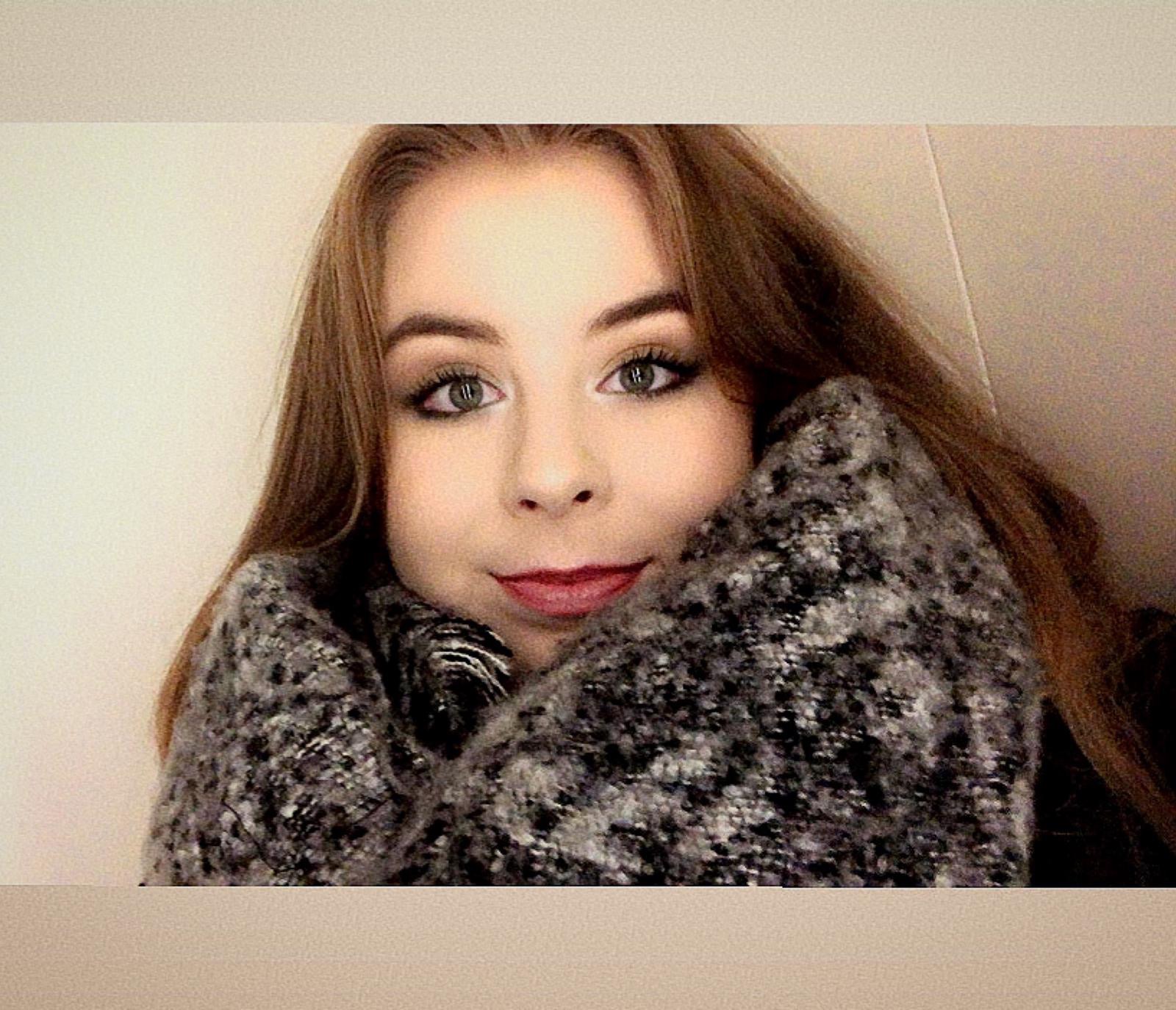 Portret młodej kobiety z długimi, brązowymi włosami i zielonymi oczami, otulonej szarym, wzorzystym szalem.