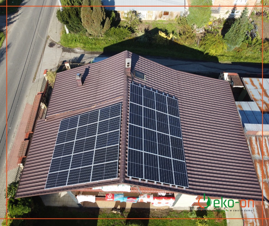 Widok z góry na brązowy dach z dwoma panelami słonecznymi, jeden większy od drugiego, z logo firmy instalacyjnej widocznym na dole zdjęcia.