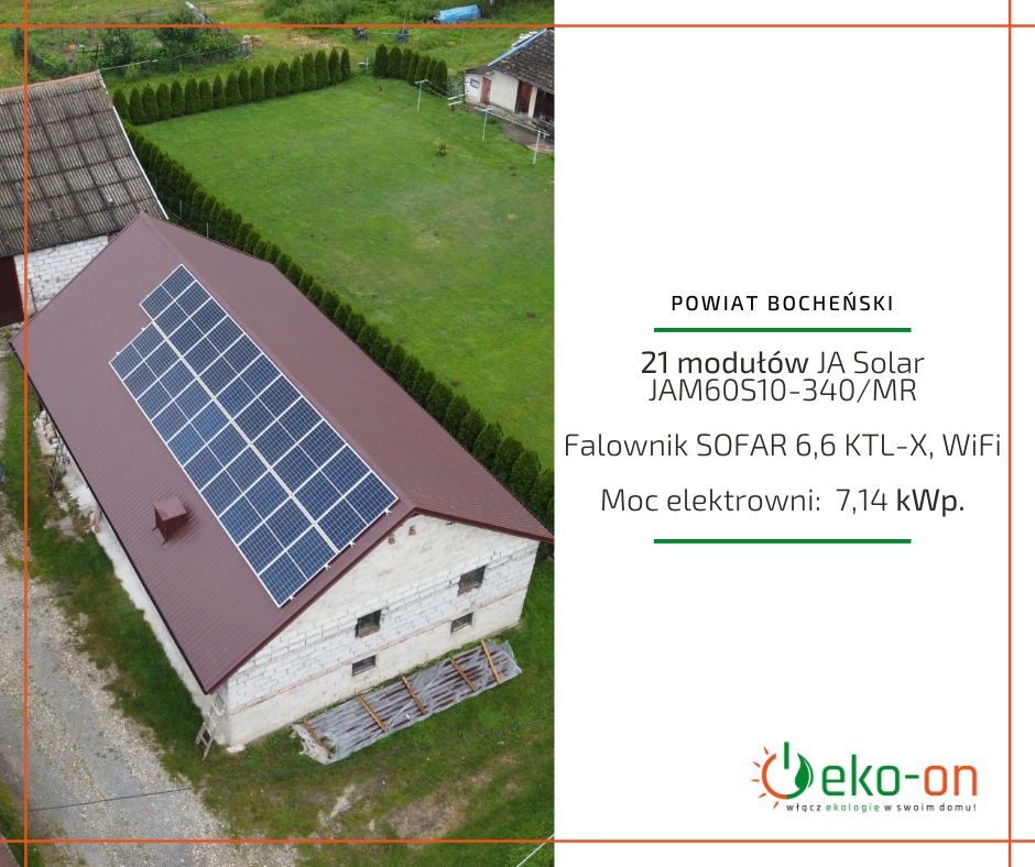 Widok z góry na budynek gospodarczy z brązowym dachem, na którym zamontowano panele słoneczne; w tle zielony trawnik i rząd tuj.