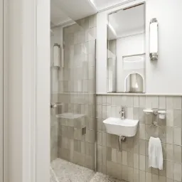 Nowoczesna łazienka z prysznicem za szklaną ścianką, umywalką na ścianie i okrągłym lustrem z oświetleniem LED, utrzymana w jasnej kolorystyce.