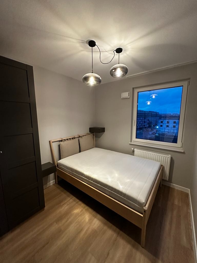 Jasne panele podłogowe w sypialni z drewnianym łóżkiem, szarą ścianą i wiszącymi lampami kulistymi.