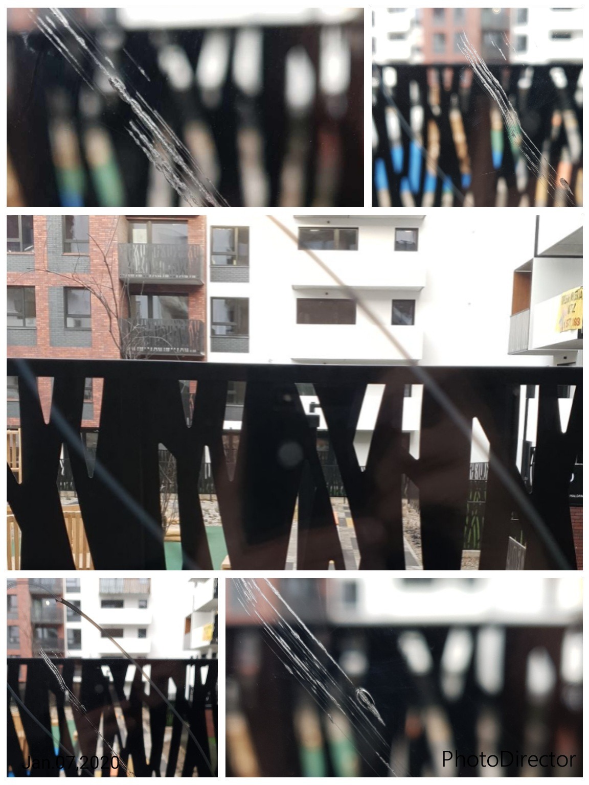 Porysowana szyba okienna z widocznymi zadrapaniami na tle zabudowy miejskiej z balkonami i elementami placu zabaw w tle, sfotografowana z bliska.