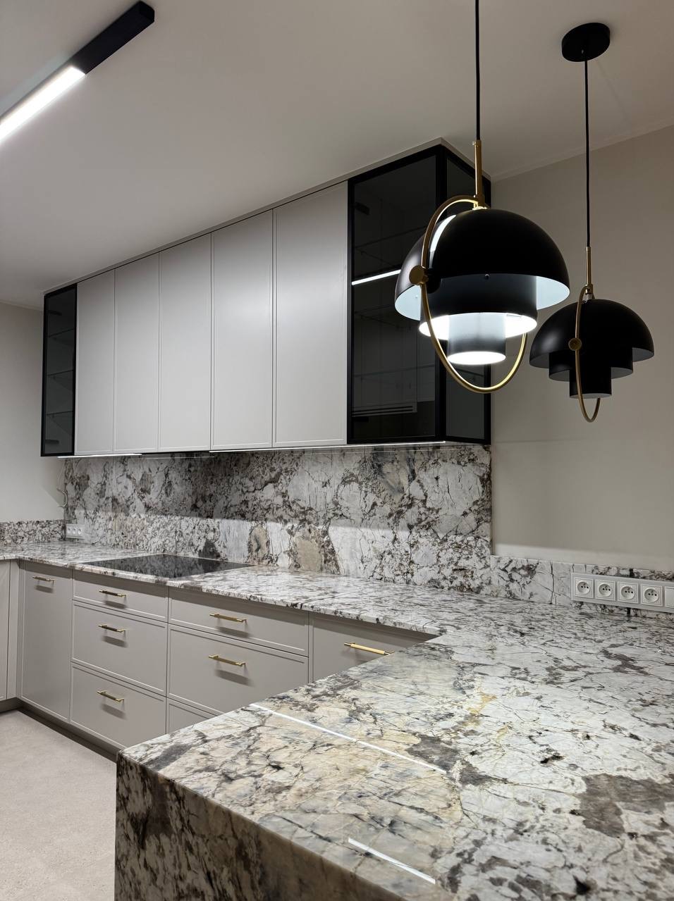 Wykończona kuchnia z szarymi szafkami, blatem z granitu Alaska White i czarnymi lampami wiszącymi o nowoczesnym designie.