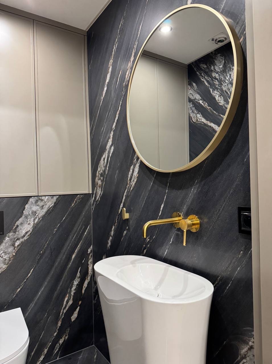 Nowoczesna łazienka z umywalką wolnostojącą, złotą armaturą i lustrem w złotej ramie na tle ściany z czarnego marmuru z białymi żyłami.
