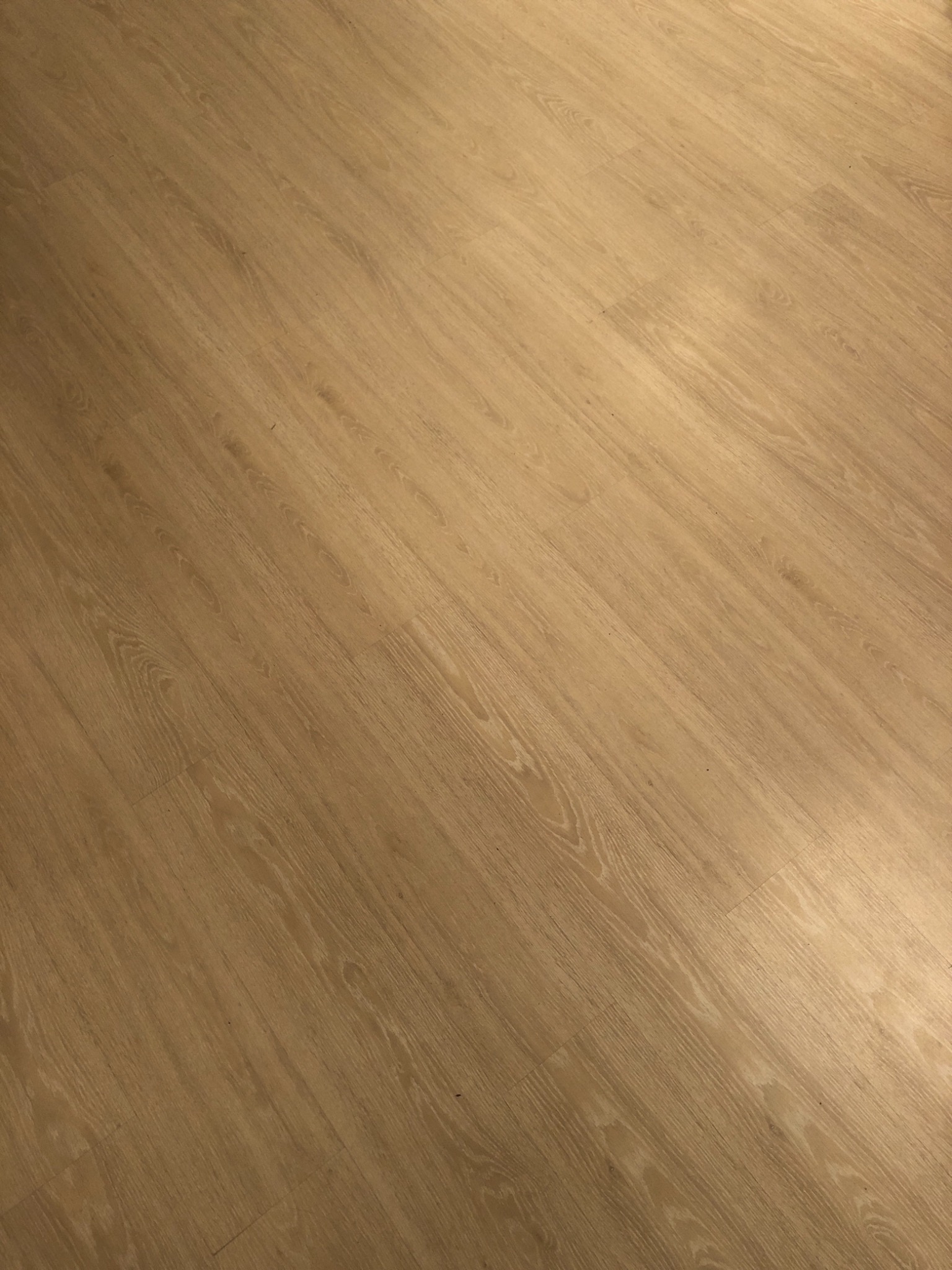 Jasna podłoga laminowana ułożona pod kątem, widoczne łączenia paneli i delikatny wzór drewna.