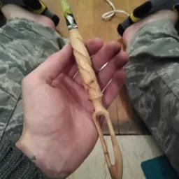 Ręcznie rzeźbiona drewniana szpatułka z Białegostoku, z charakterystycznym spiralnym uchwytem i rozwidlonym zakończeniem, trzymana w dłoni na tle podłogi.