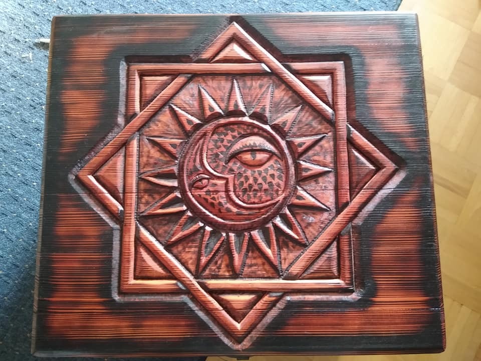 Drewniana skrzynia z rzeźbionym motywem słońca, księżyca i oka, wykończona techniką opalania drewna.
