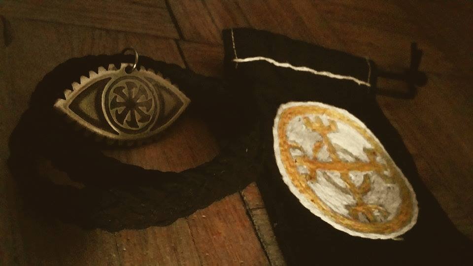 Czarny woreczek z haftowanym ornamentem obok zawieszki w kształcie oka z metalu na drewnianym podłożu.