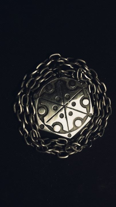 Metalowy medalion z geometrycznym wzorem otoczony łańcuchem na ciemnym tle.