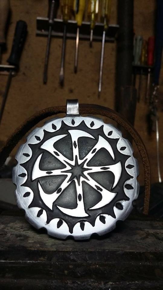 Ręcznie wykonany srebrny wisiorek z symbolem słowiańskim na skórzanym rzemyku, widoczny na tle warsztatu z narzędziami.