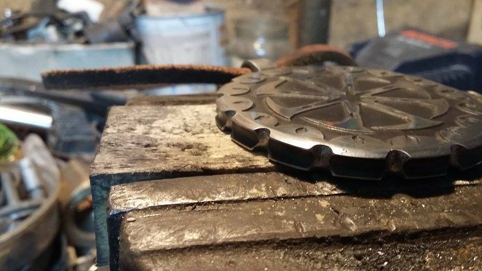 Metalowy, okrągły element z wygrawerowanym wzorem w imadle, w tle widoczne narzędzia i materiały warsztatowe.