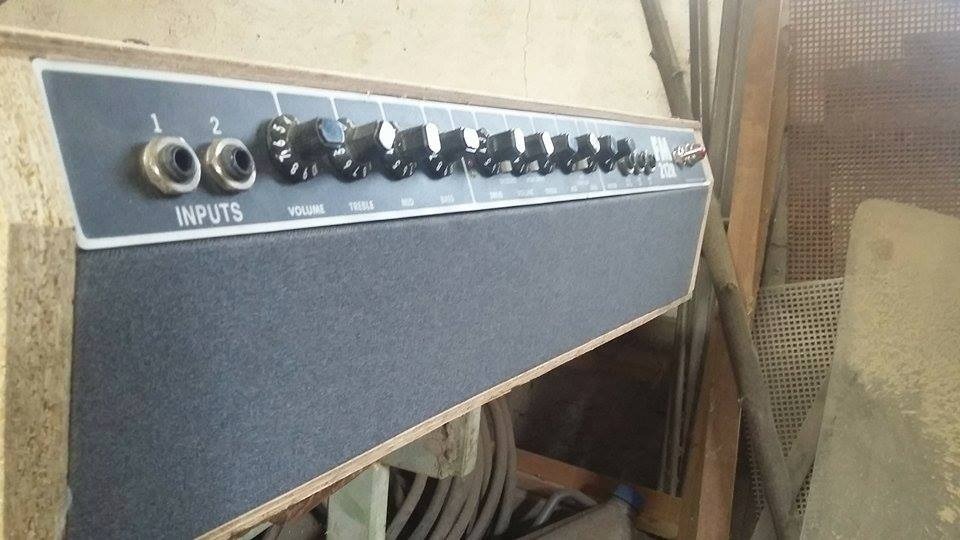 Niedokończona obudowa wzmacniacza gitarowego z surowego drewna i czarnym panelem przednim z potencjometrami, widoczna w warsztacie stolarskim.