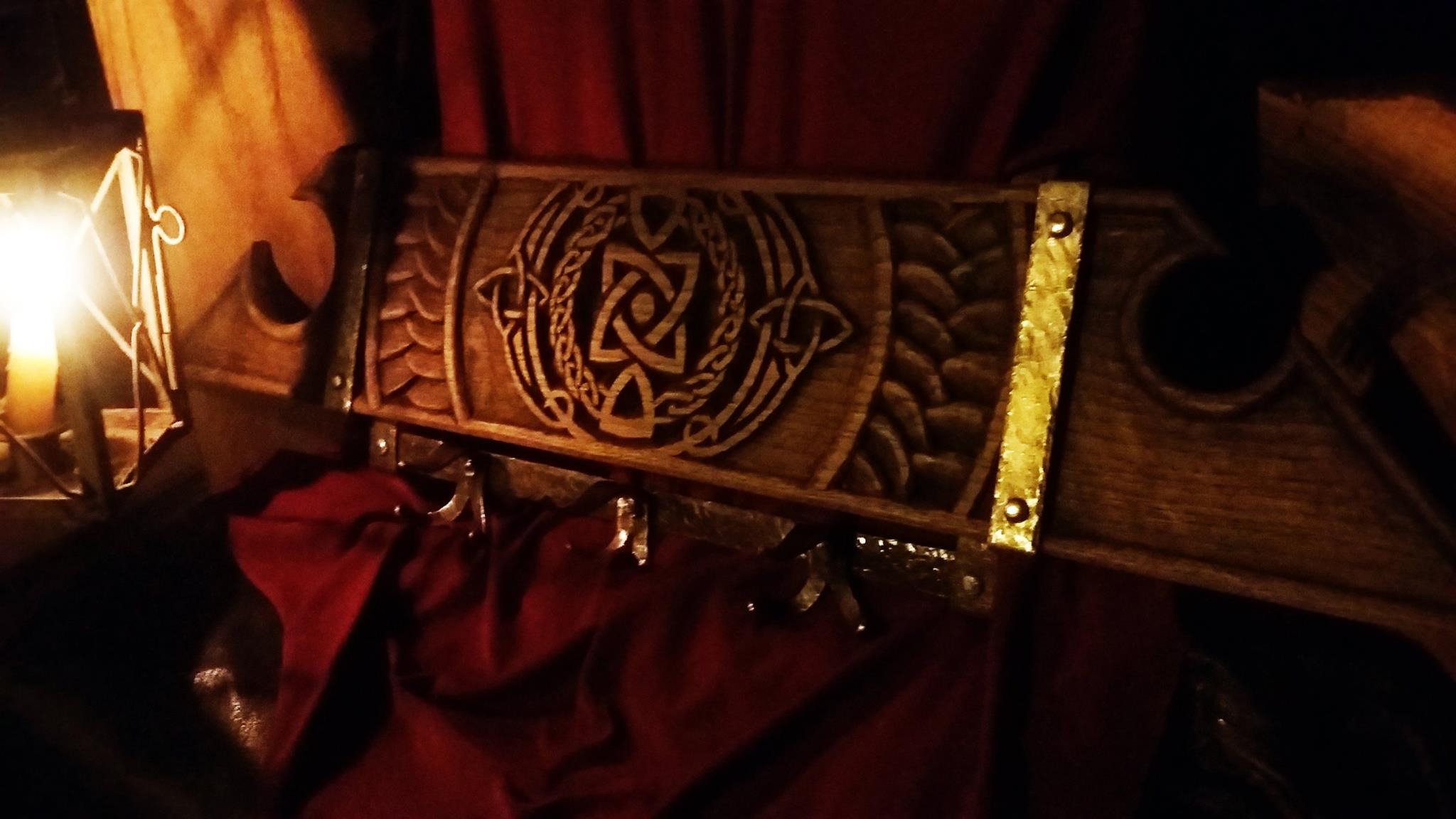 Drewniana skrzynia z wygrawerowanym celtyckim wzorem, zdobiona złotymi elementami, oświetlona ciepłym światłem lampki.