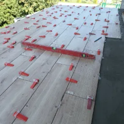 Układanie płytek podłogowych z użyciem poziomicy i czerwonych klinów dystansowych na zewnątrz budynku.