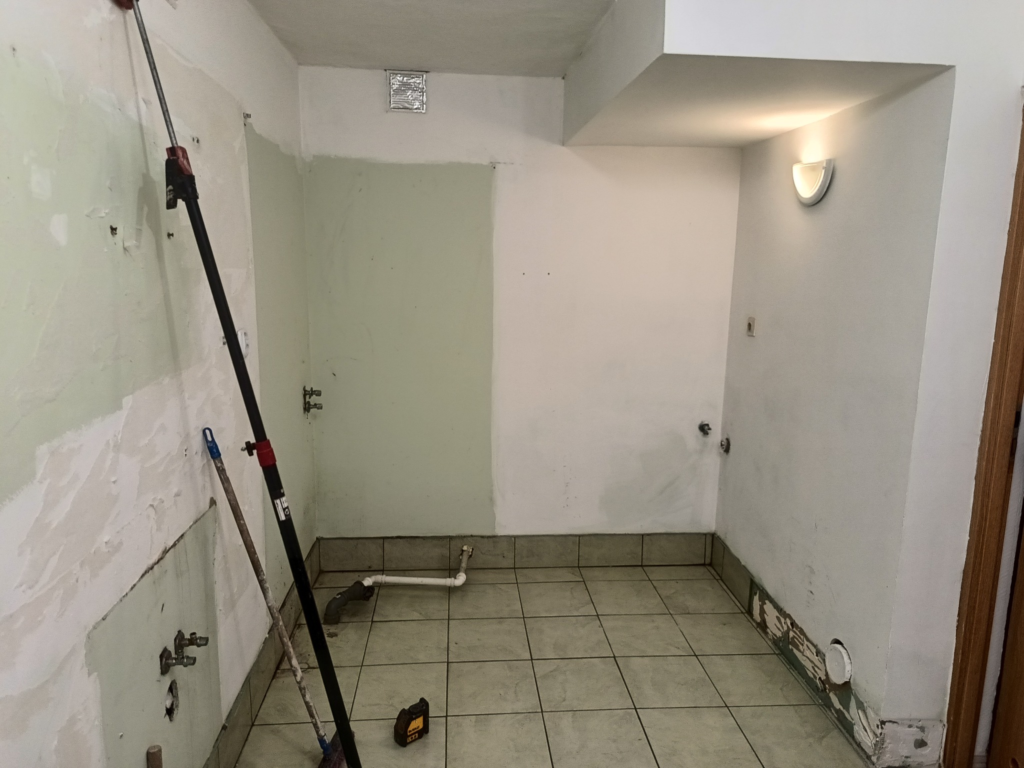 Łazienka w trakcie remontu: ściany częściowo przygotowane do malowania, widoczne rury, narzędzia malarskie i poziomica laserowa na podłodze.