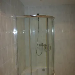 Kabina prysznicowa narożna z hydromasażem, obudowana jasnymi płytkami ceramicznymi, oświetlona trzema punktowymi lampami sufitowymi.