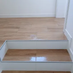 Schody wykończone panelami imitującymi drewno, z białymi podstopnicami i srebrnymi listwami krawędziowymi, w mieszkaniu w Żorach.