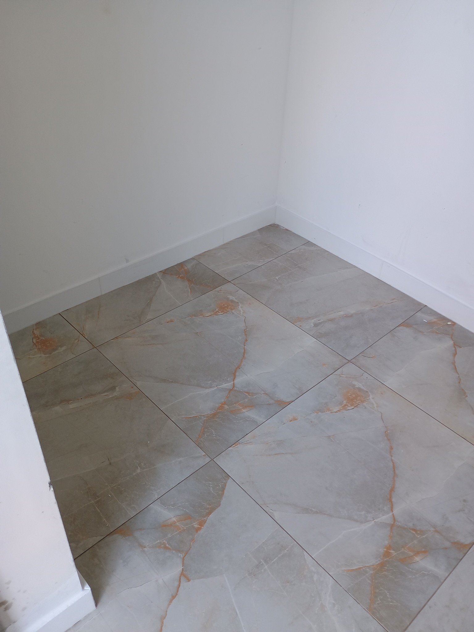 Ułożone płytki podłogowe imitujące marmur w narożniku pomieszczenia z białymi ścianami i przypodłogowymi listwami.