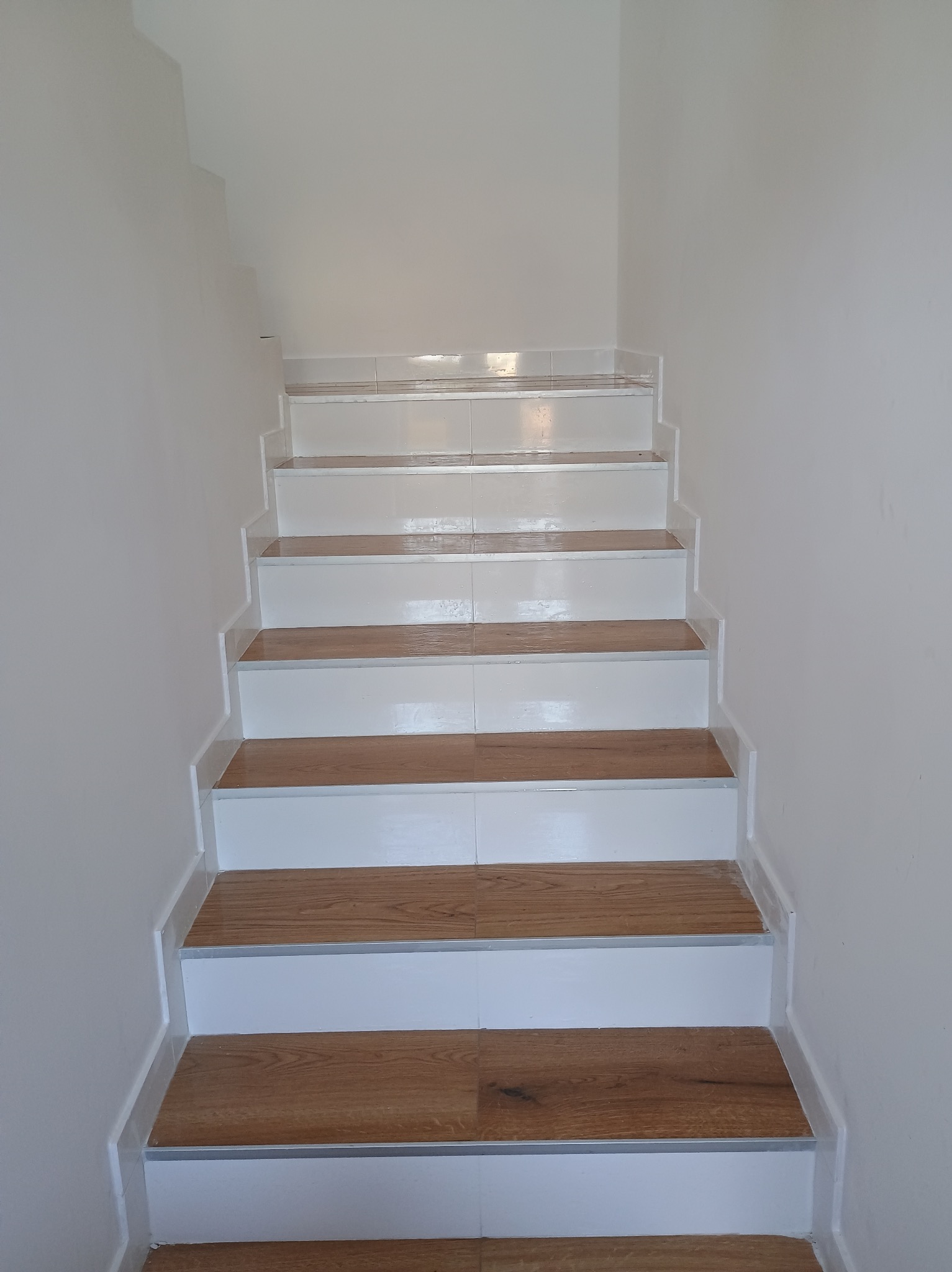 Schody wykończone panelami drewnopodobnymi z białymi podstopnicami i listwami przypodłogowymi, widok z dołu.