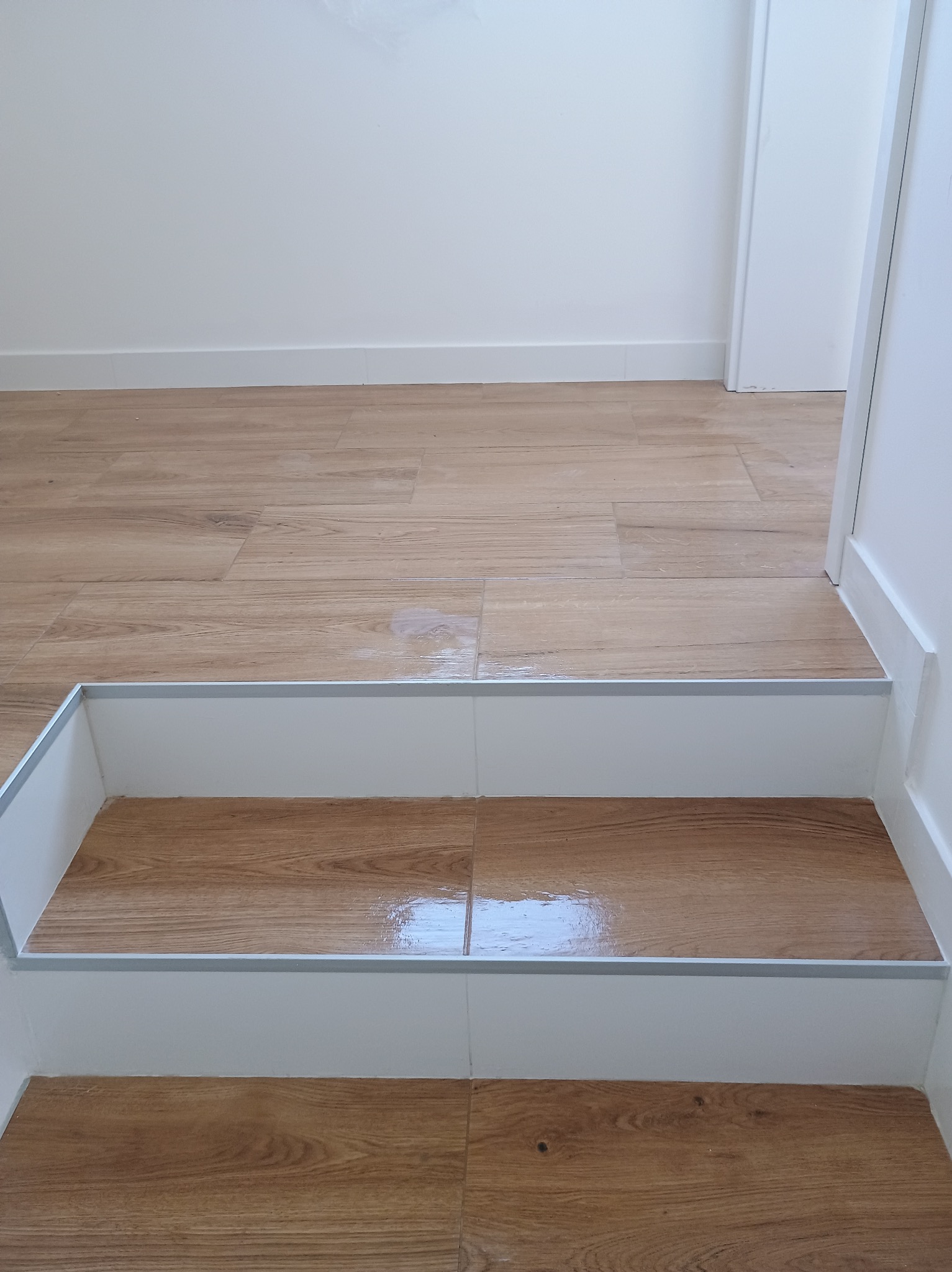 Schody wykończone panelami imitującymi drewno, z białymi podstopnicami i srebrnymi listwami krawędziowymi, w mieszkaniu w Żorach.