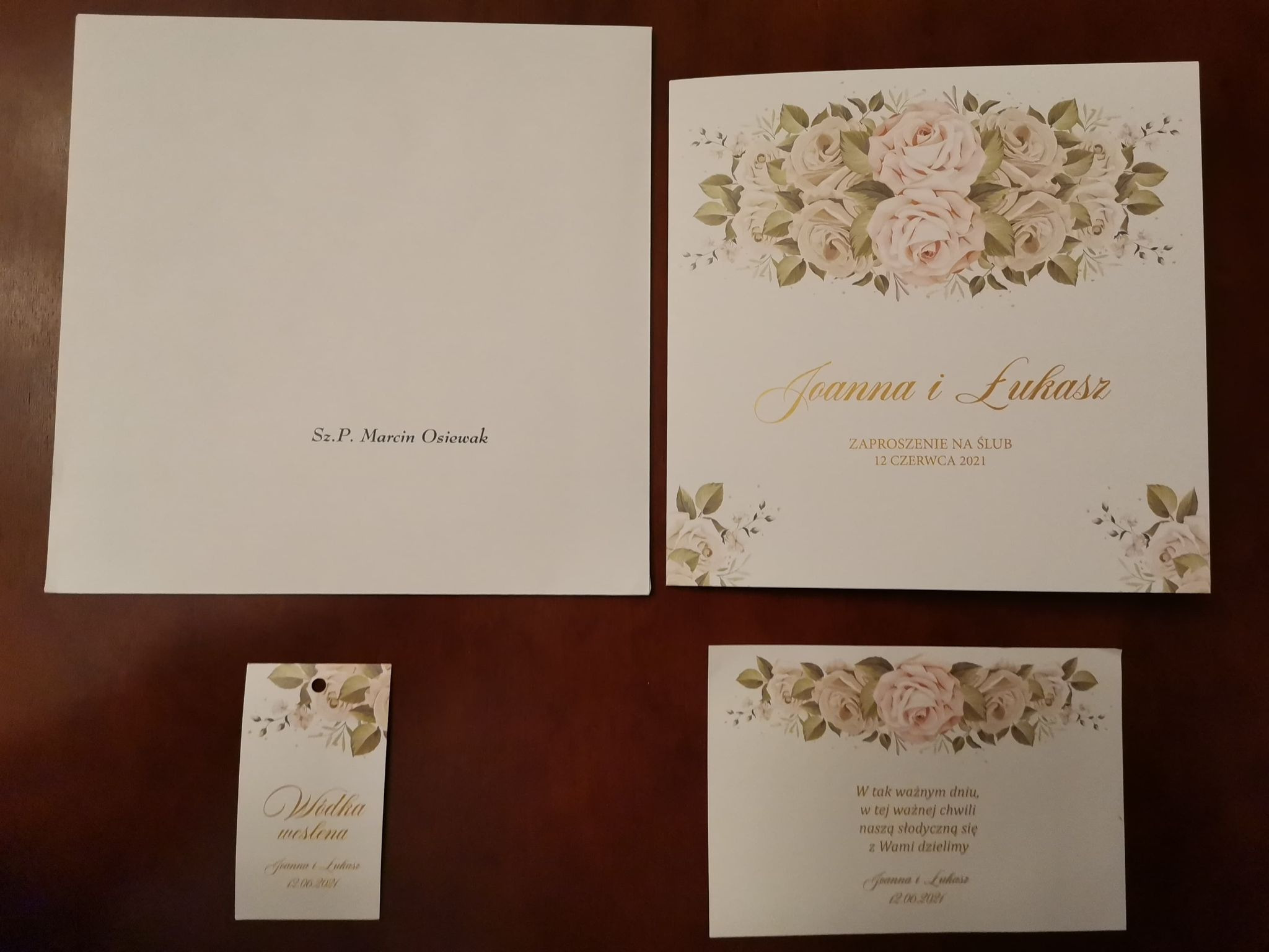 Komplet papeterii ślubnej: zaproszenie, winietka na alkohol i kartka z podziękowaniem dla gości, utrzymane w kremowej kolorystyce z motywem róż i zielonych listków.