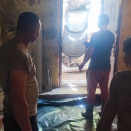 Tech House Tomasz Hauser - Ekipa remontowa wprowadza maszynę do wylewki posadzek do pomieszczenia zabezpieczonego folią. Widoczne ściany w trakcie prac przygotowawczych.