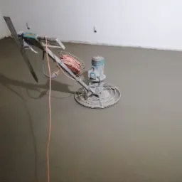 Zacieraczka mechaniczna do posadzek w trakcie pracy na świeżo wylanym jastrychu cementowym w pomieszczeniu z białymi ścianami.