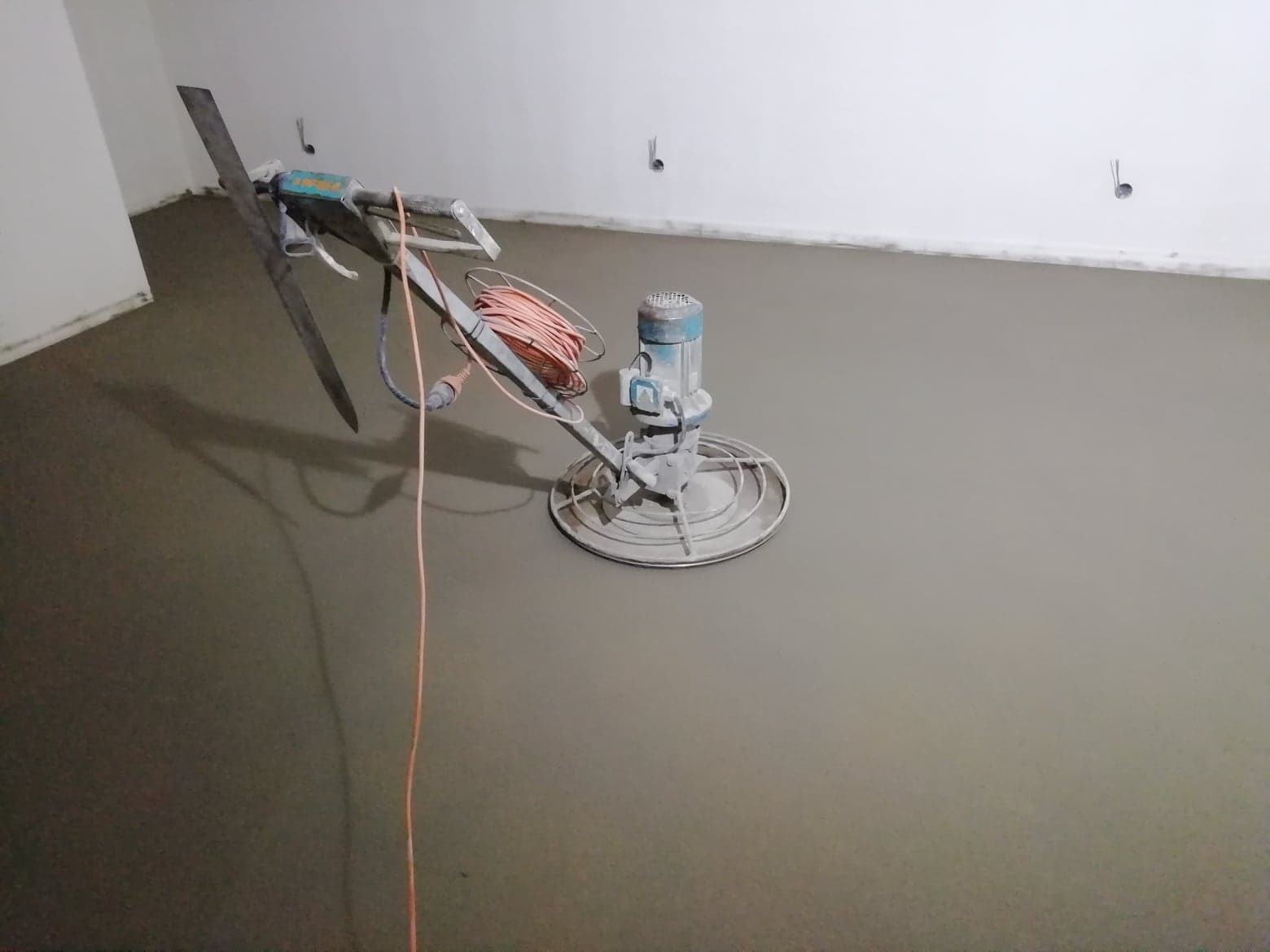 Zacieraczka mechaniczna do posadzek w trakcie pracy na świeżo wylanym jastrychu cementowym w pomieszczeniu z białymi ścianami.
