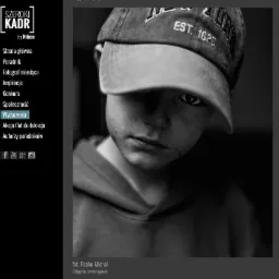 Portret czarno-biały chłopca w bluzie z kapturem i czapce z daszkiem zasłaniającej część twarzy, z jednym okiem widocznym i zamyślonym wyrazem twarzy.